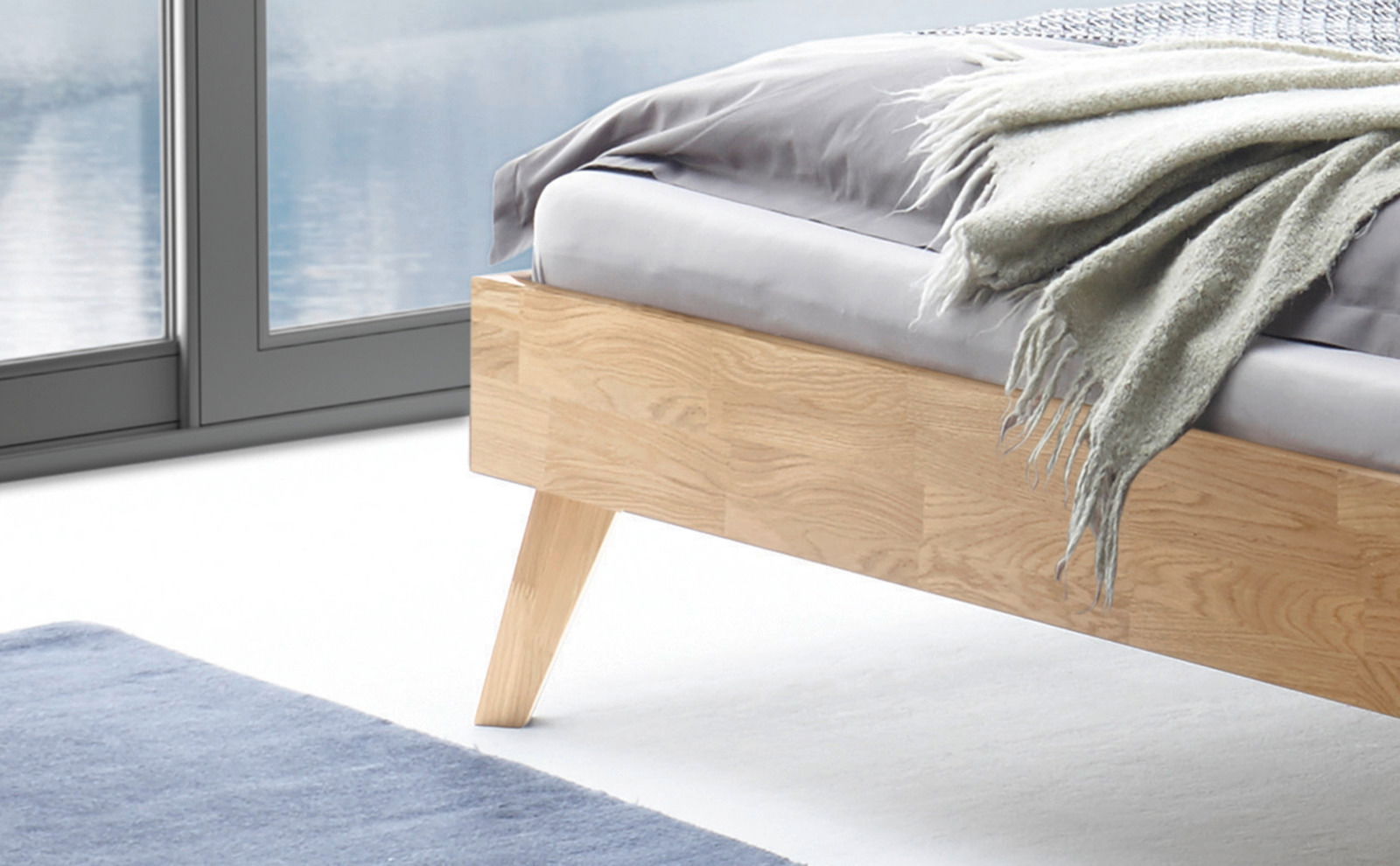 Nahaufnahme eines modernen Bettgestells aus hellem Holz mit schrägen Beinen, seitliche Perspektive