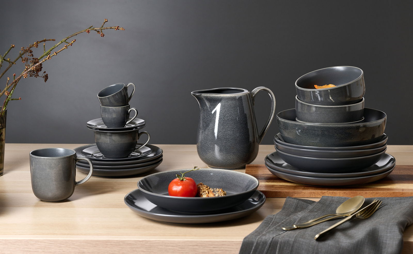 Ritzenhoff & Breker Speiseteller TOLEDO Elegantes, dunkelgraues Geschirrset mit Tellern, Tassen und Schalen, auf einem Holztisch arrangiert. Perspektive von vorne.