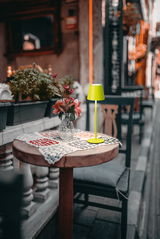 Akku-Tischleuchte VILETTO in leuchtendem Grün auf einem runden Holztisch mit Blumenstrauß, seitliche Perspektive.