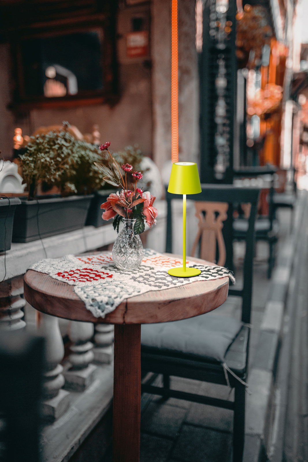 Akku-Tischleuchte VILETTO in leuchtendem Grün auf einem runden Holztisch mit Blumenstrauß, seitliche Perspektive.