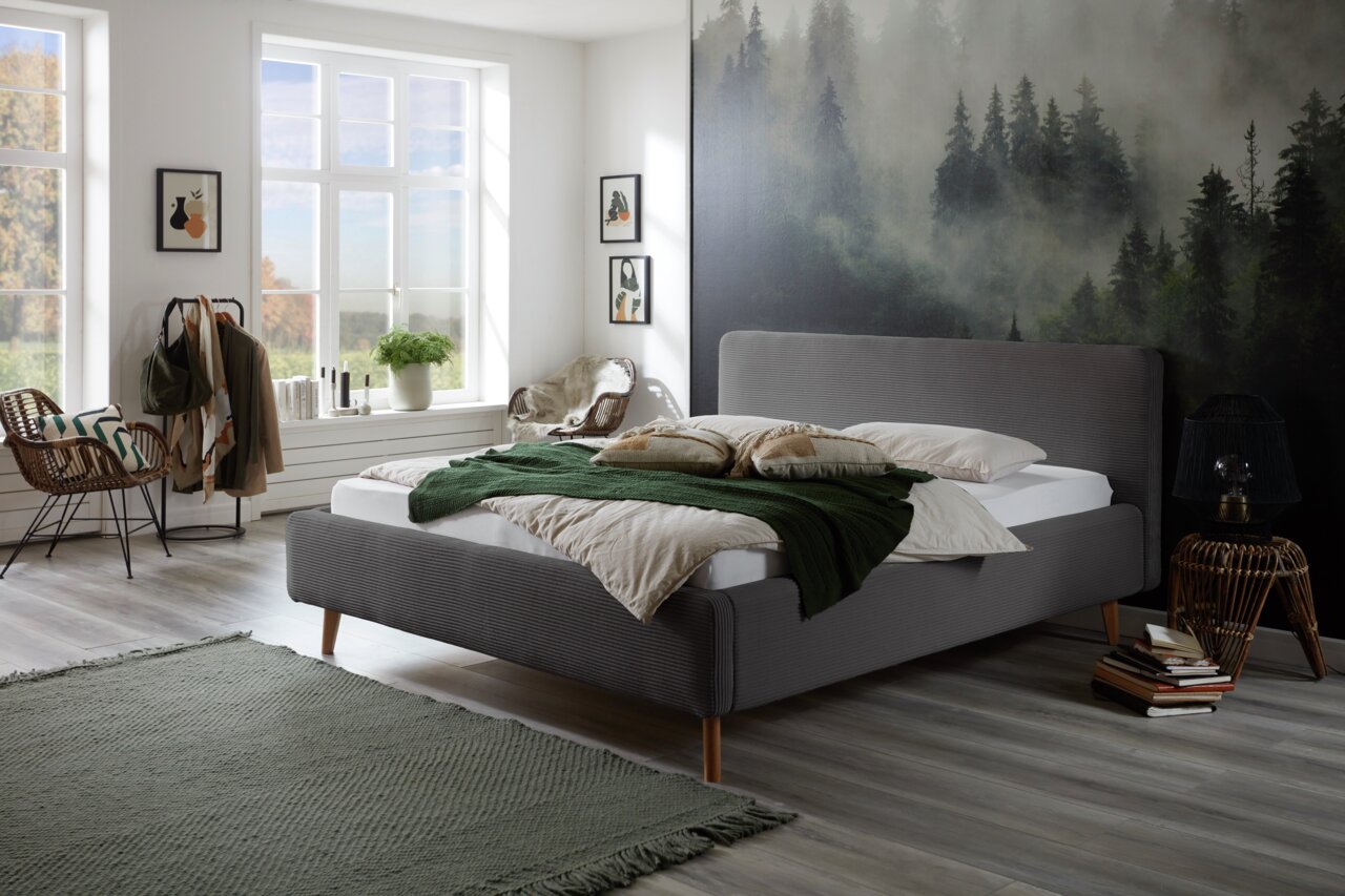Modernes Polsterbett in einem stilvoll eingerichteten Schlafzimmer mit Waldbild an der Wand, seitliche Perspektive.