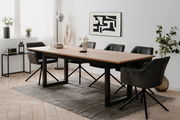 Moderner Esstisch mit Holzplatte und schwarzen Metallbeinen, umgeben von schwarzen Stühlen in einem hellen Raum mit Kunst an der Wand, aus seitlicher Perspektive.