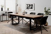 Moderner Esstisch mit Holzplatte und schwarzen Metallbeinen, umgeben von schwarzen Stühlen in einem hellen Raum mit Kunst an der Wand, aus seitlicher Perspektive.