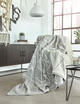 Gemütliche Jacquard Decke in modernem geometrischen Muster, drapiert über einem Sessel in einem stilvollen Wohnzimmer mit Blick auf ein großes Fenster.