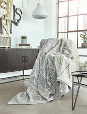 Gemütliche Jacquard Decke in modernem geometrischen Muster, drapiert über einem Sessel in einem stilvollen Wohnzimmer mit Blick auf ein großes Fenster.