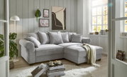 Gemütliche graue Eckcouch in einem hellen Wohnzimmer mit großen Fenstern, dekoriert mit Kissen und einer Decke, seitliche Perspektive.