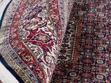 Nahaufnahme eines Orientteppichs mit detailliertem floralen Muster in Rot, Blau und Beige, teilweise aufgerollt.