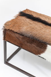 Bank mit braun-weißem Fellbezug und Metallrahmen, seitliche Perspektive