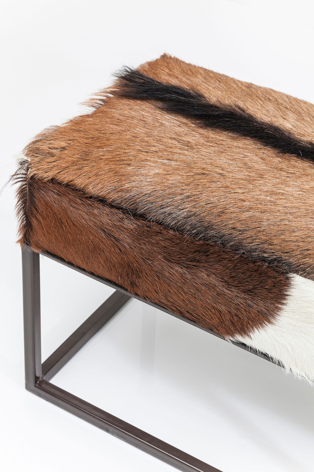 Bank mit braun-weißem Fellbezug und Metallrahmen, seitliche Perspektive