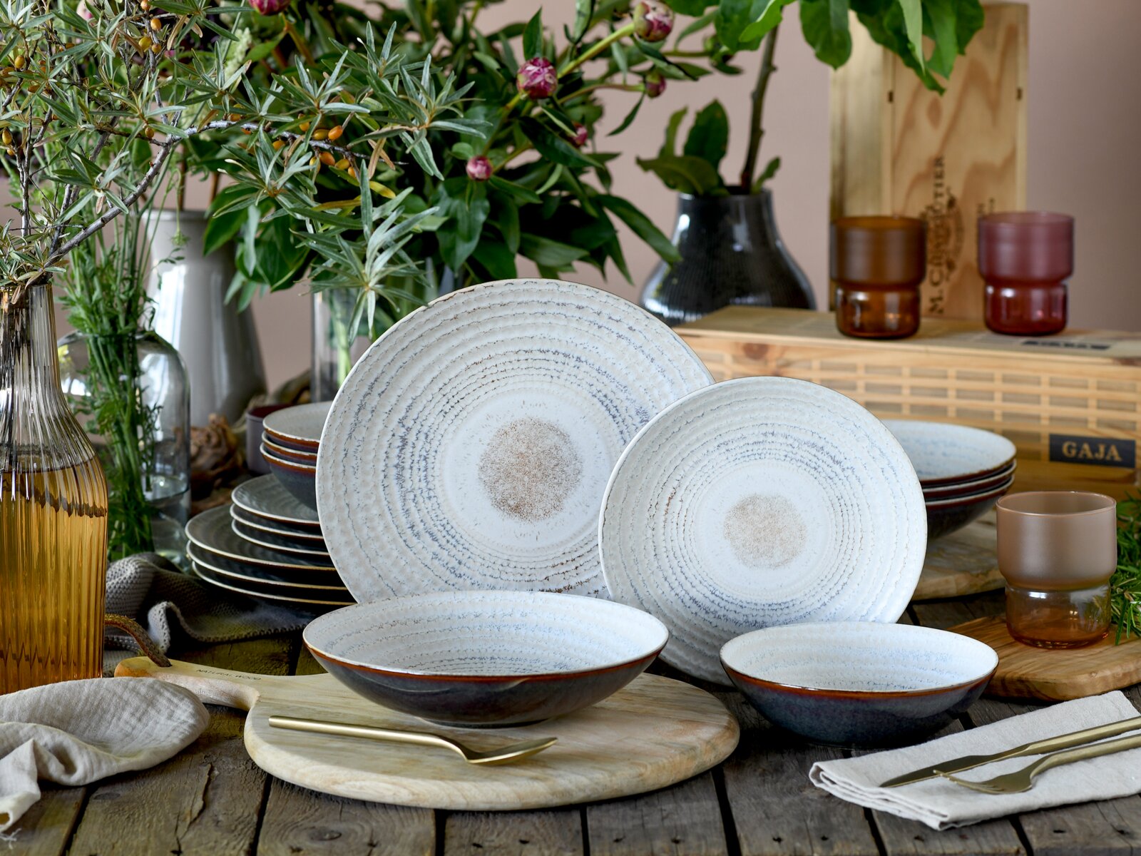 Creatable Tellerset 16-tlg NEAPEL Rustikales Keramik-Geschirrset mit großen und kleinen Tellern sowie Schalen in Weiß-Blau mit konzentrischem Muster, dekorativ auf Holztisch arrangiert, Frontansicht in leicht erhöhter Perspektive.