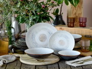 Rustikales Keramik-Geschirrset mit großen und kleinen Tellern sowie Schalen in Weiß-Blau mit konzentrischem Muster, dekorativ auf Holztisch arrangiert, Frontansicht in leicht erhöhter Perspektive.