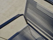 Nahaufnahme eines Stapelsessels mit blauen Armlehnen und grauen Seilbespannungen, von oben betrachtet.