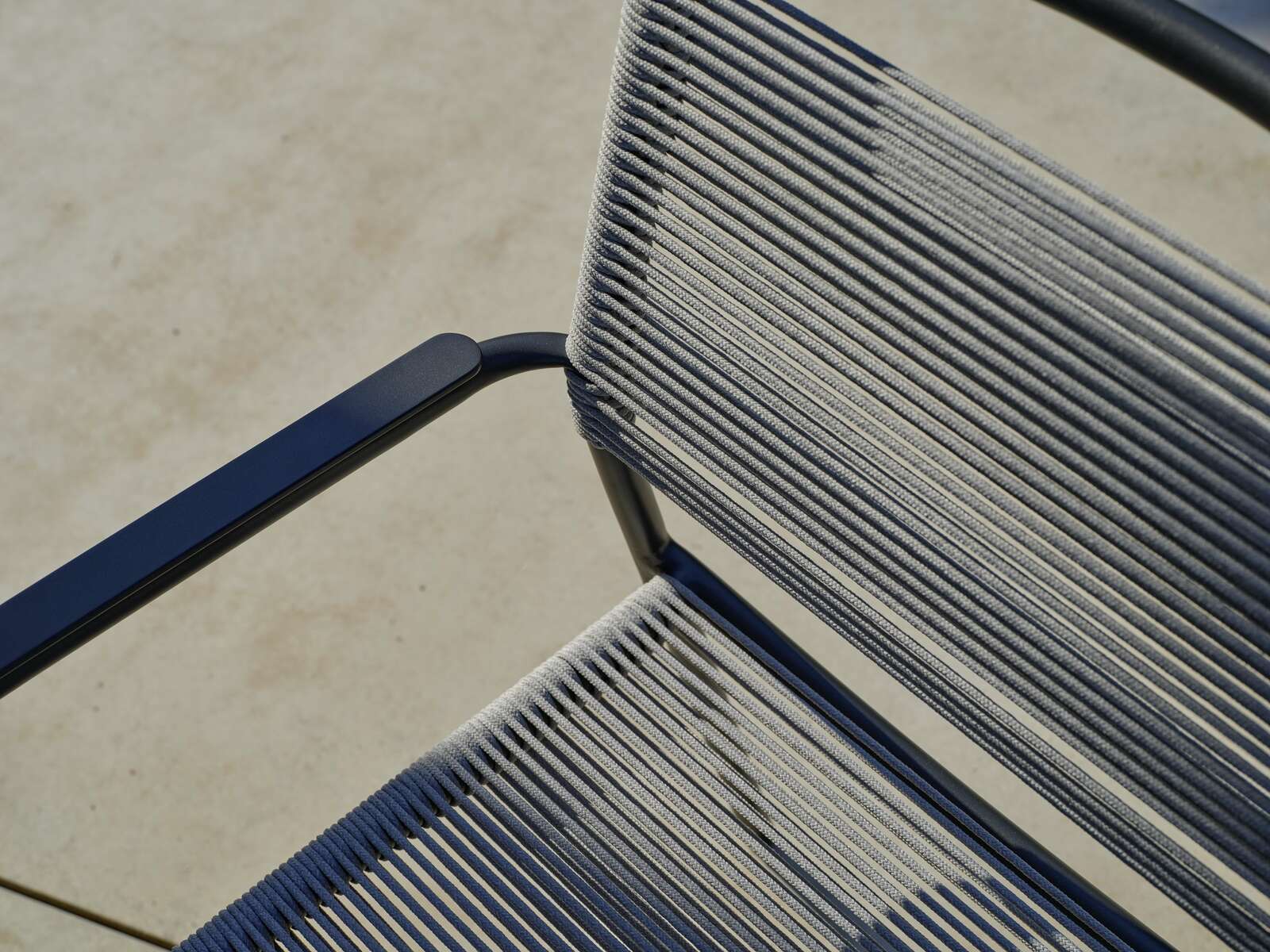 Nahaufnahme eines Stapelsessels mit blauen Armlehnen und grauen Seilbespannungen, von oben betrachtet.