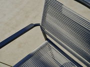 Nahaufnahme eines Stapelsessels mit blauen Armlehnen und grauen Seilbespannungen, von oben betrachtet.