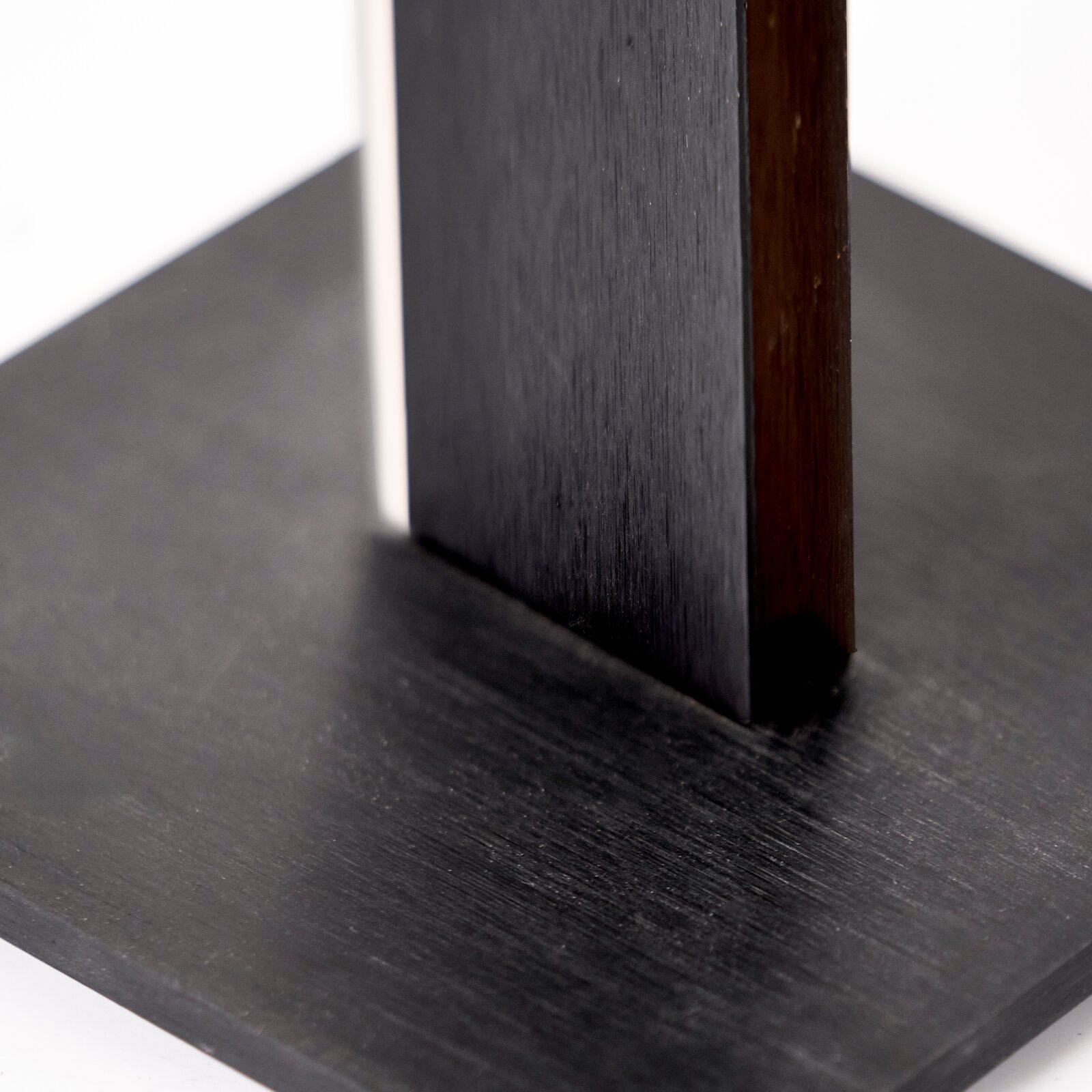 Detailansicht aus schräger Perspektive auf eine schwarze quadratische Holzplatte mit zwei senkrechten, dunkel lackierten Holzelementen