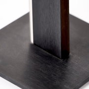 Detailansicht aus schräger Perspektive auf eine schwarze quadratische Holzplatte mit zwei senkrechten, dunkel lackierten Holzelementen