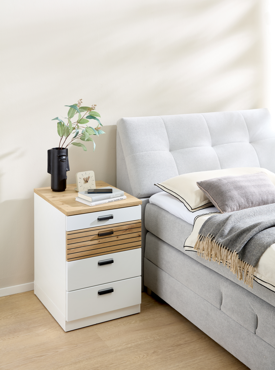 Rollcontainer GLENN in einem modernen Schlafzimmer, seitliche Perspektive, mit drei Schubladen und dekorativen Gegenständen auf der Oberseite.