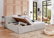 Modernes, hellgrau gepolstertes Bett mit hochgeklapptem Lattenrost und geräumigem Bettkasten, aus schräger Vorderansicht in einem hellen Schlafzimmer gezeigt