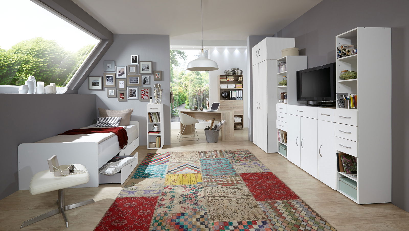 Modernes Schlafzimmer mit Schreibtisch, Bett und Stauraummöbeln in heller, freundlicher Atmosphäre. Perspektive von der Seite mit Blick auf das gesamte Zimmer.