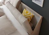 Beige Boxspringbett mit gepolstertem Kopfteil und gelbem Zierkissen, seitliche Perspektive