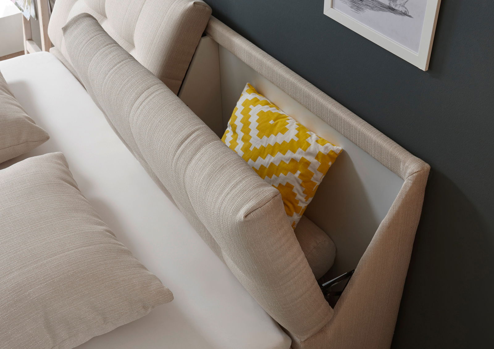 Beige Boxspringbett mit gepolstertem Kopfteil und gelbem Zierkissen, seitliche Perspektive
