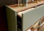 Detailansicht aus schräger Vogelperspektive auf ein geöffnetes Sideboard in Salbeigrün mit Holzplatte, strukturierter Schubladeneinlage und offenen Ablagefächern