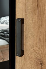 Nahaufnahme eines Türgriffs an einem Drehtürenschrank aus Holz mit Metallakzenten, seitliche Perspektive.