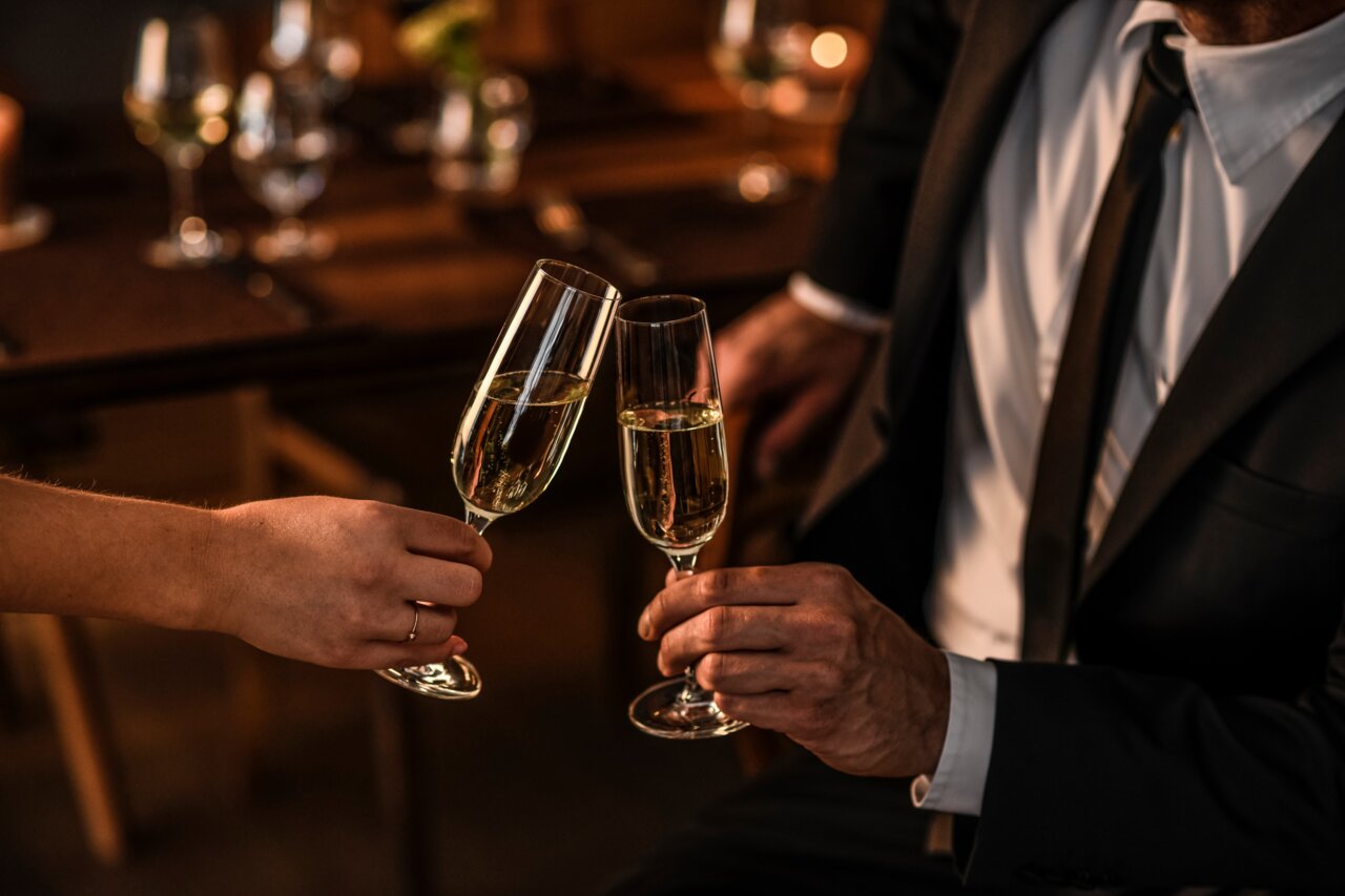 Zwei Personen stoßen mit Sektgläsern an, elegante Abendatmosphäre, seitliche Perspektive
