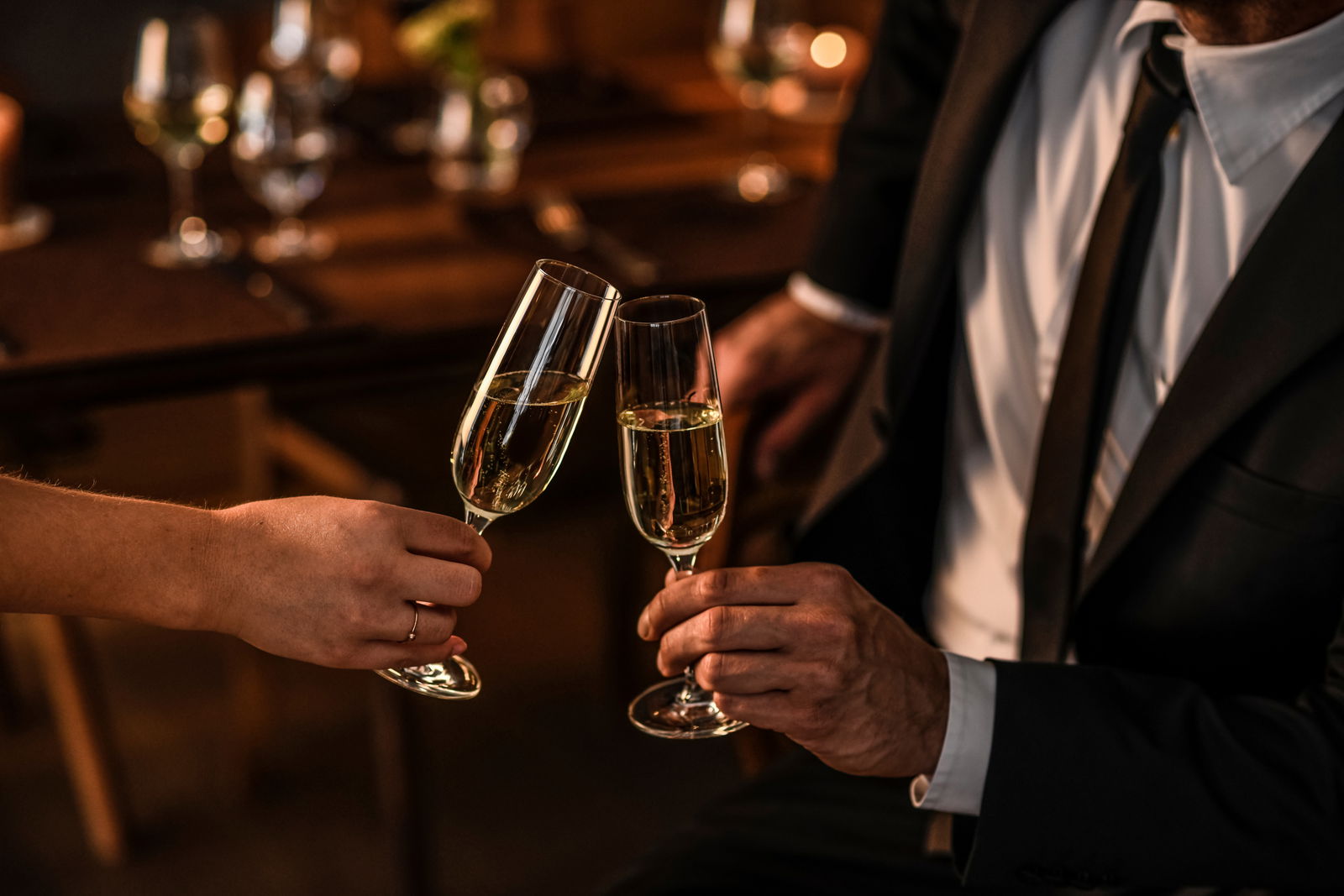 Zwei Personen stoßen mit Sektgläsern an, elegante Abendatmosphäre, seitliche Perspektive