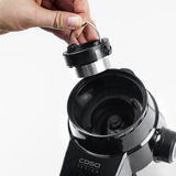 Nahaufnahme einer Kaffeemühle von oben, bei der ein Teil des Mahlwerks von einer Hand gehalten wird.