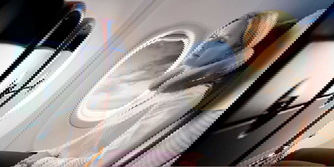 Frau schläft im Flugzeug mit grauem Nackenkissen