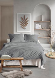 Graue Bettwäsche in einem modernen Schlafzimmer mit dekorativem Wandbild und Regal im Hintergrund, aus der Perspektive von vorne.