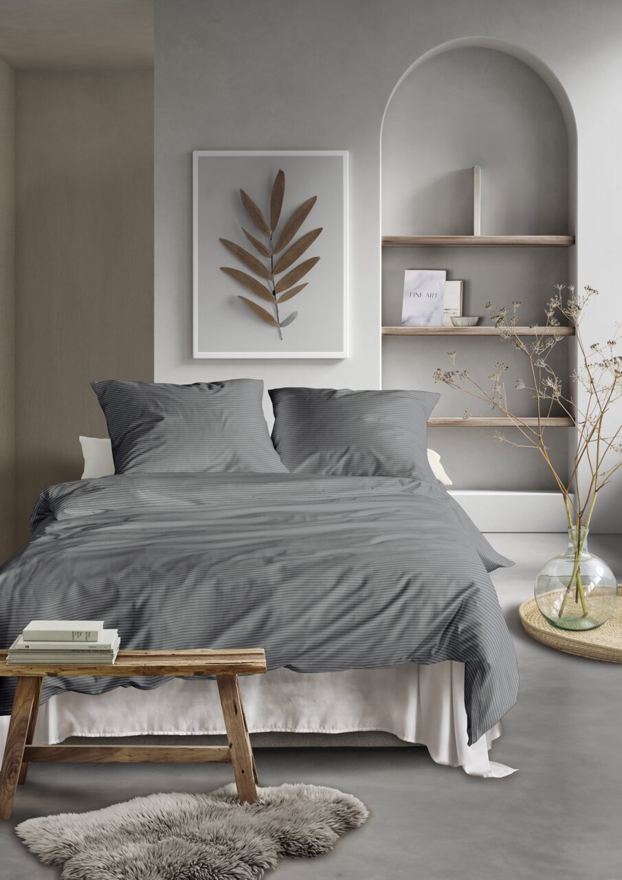Graue Bettwäsche in einem modernen Schlafzimmer mit dekorativem Wandbild und Regal im Hintergrund, aus der Perspektive von vorne.