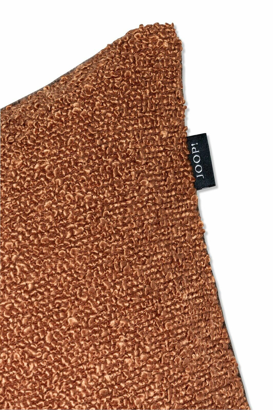 Nahaufnahme einer braunen Zierkissenhülle mit strukturierter Oberfläche und einem schwarzen Etikett mit der Aufschrift 'JOOP!'