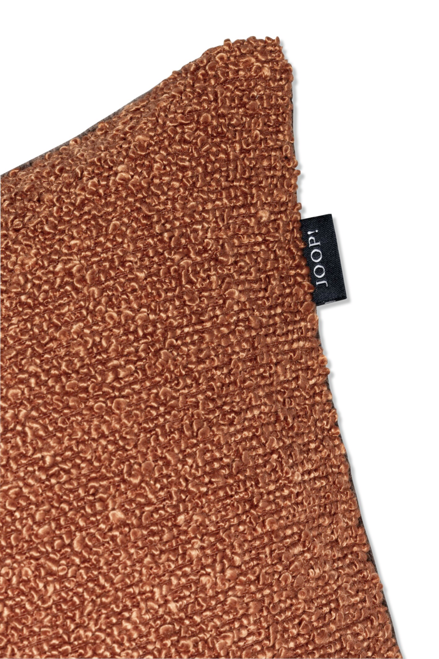 Nahaufnahme einer braunen Zierkissenhülle mit strukturierter Oberfläche und einem schwarzen Etikett mit der Aufschrift 'JOOP!'