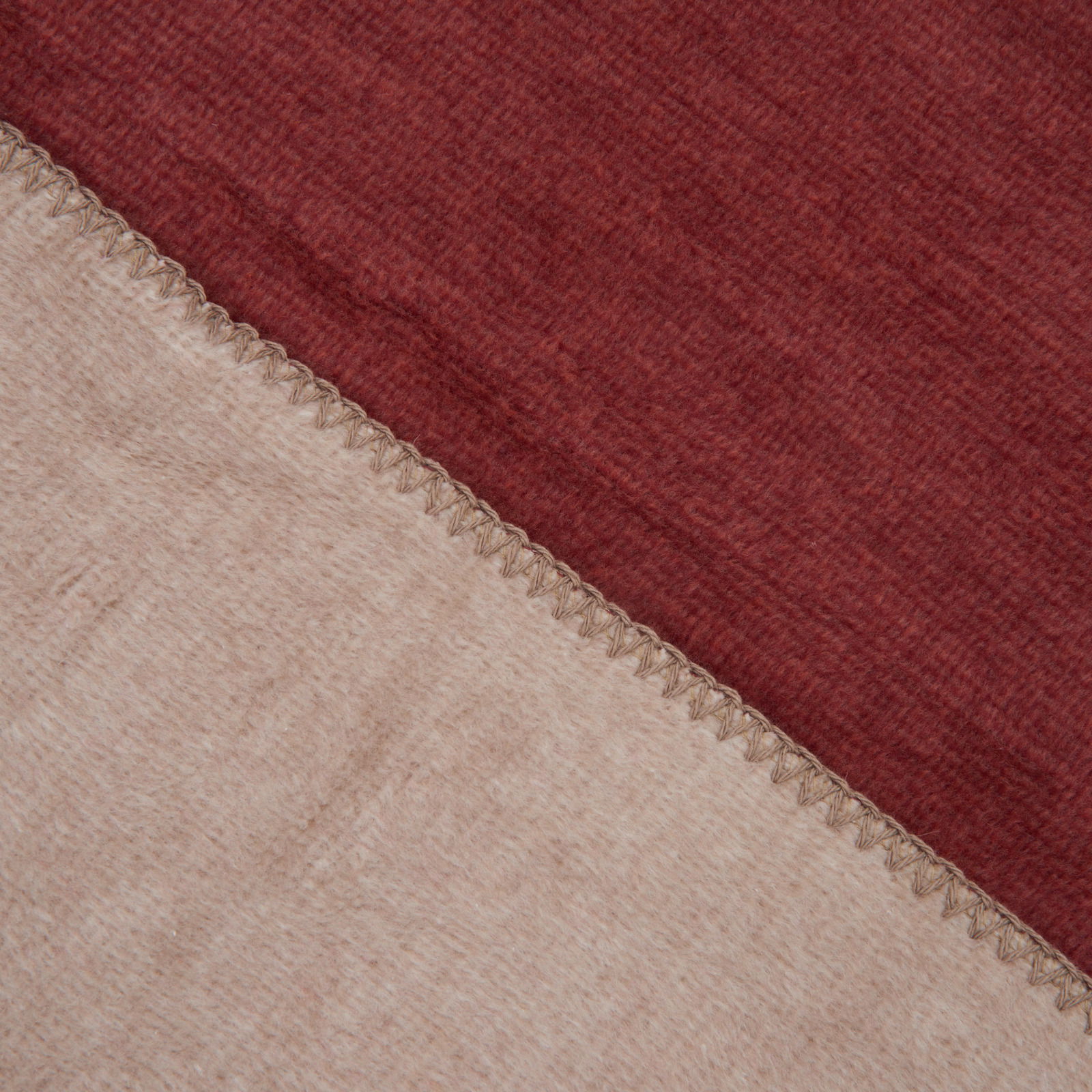 Nahaufnahme einer zweifarbigen Decke in Rot und Beige mit sichtbarer Naht, von oben betrachtet.