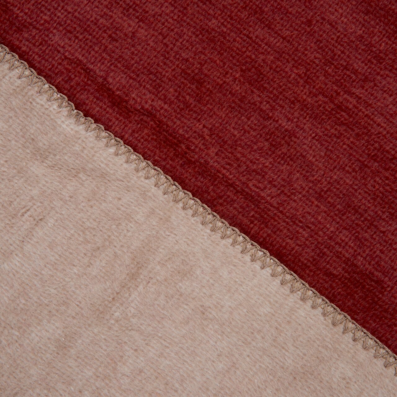 Nahaufnahme einer zweifarbigen Decke in Rot und Beige mit sichtbarer Naht, von oben betrachtet.