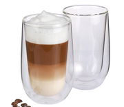 Zwei doppelwandige Latte Macchiato Gläser, eines gefüllt mit einem dreischichtigen Latte Macchiato, aus seitlicher Perspektive fotografiert.