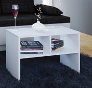 Weißer, moderner Couchtisch mit offener Ablage und Bücherfächern auf dunklem Hochflorteppich vor einem Sofa, mit Vase und Glas auf der Tischplatte, Ansicht schräg von vorne.