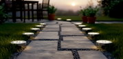 Bodennahe Perspektive: runde Solar-Bodenleuchten säumen einen Gartenweg aus Steinplatten und spenden warmweißes Licht bei Sonnenuntergang.