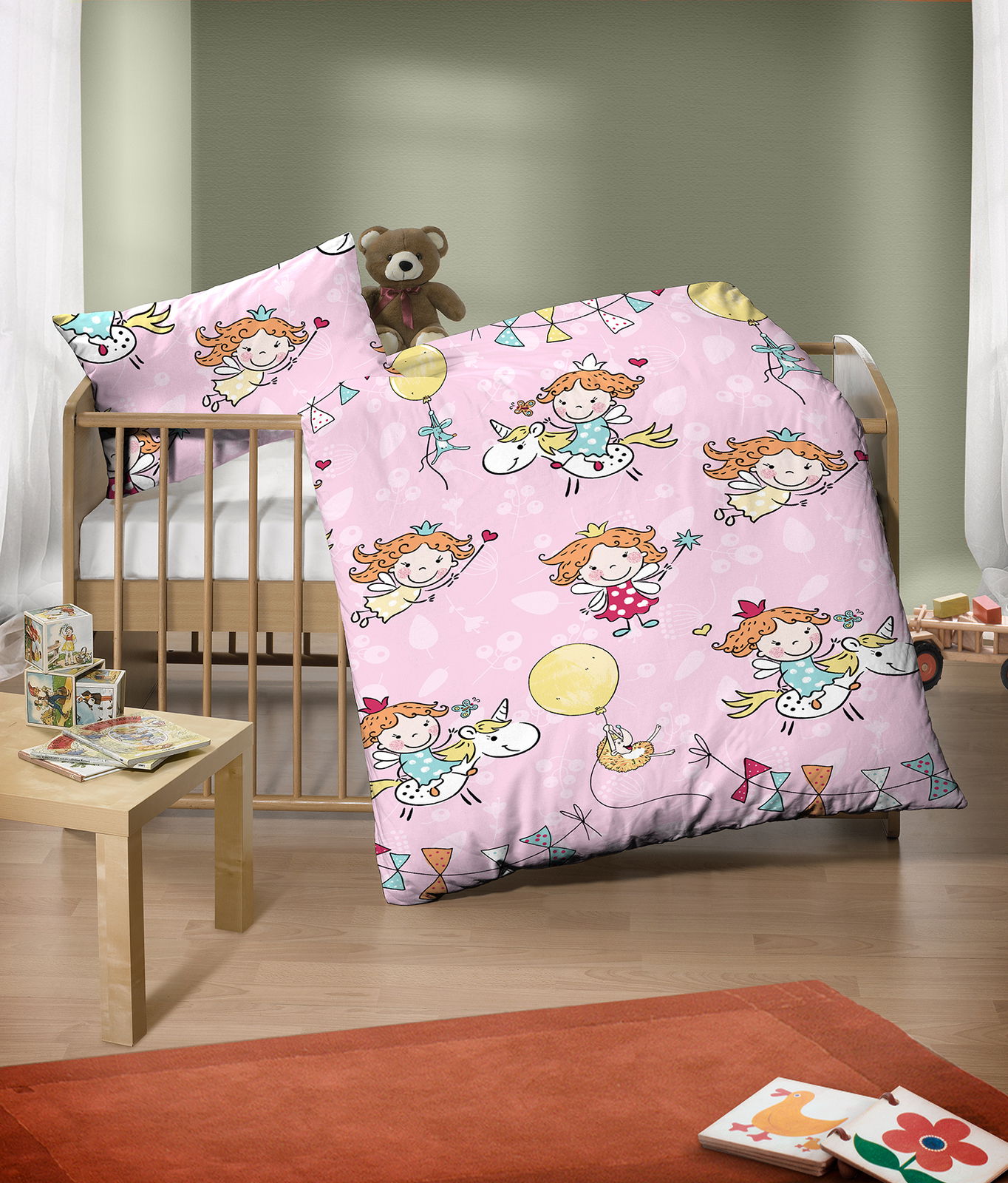 Kinderbettwäsche-Set mit fröhlichen Feen- und Einhornmotiven auf rosa Hintergrund, im Kinderzimmer mit Holzgitterbett und Kuscheltier, aus der Perspektive von vorne.