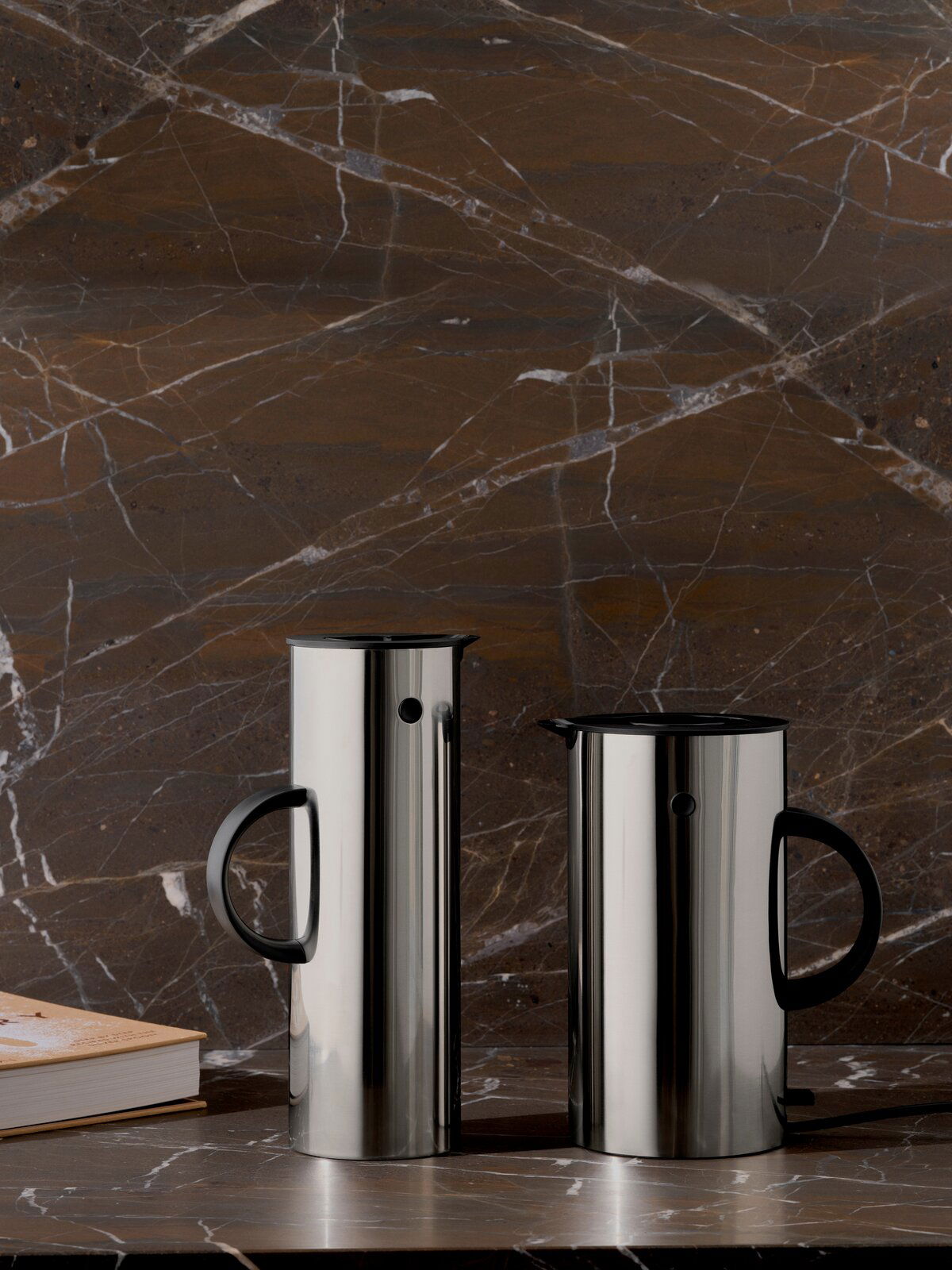 Zwei elegante Isolierkannen aus Stahl mit schwarzem Griff, auf einer Marmoroberfläche stehend, seitliche Perspektive.
