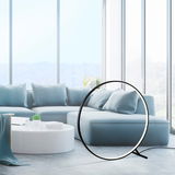 Moderne Stehleuchte HULA in Ringform, seitliche Perspektive, in einem hellen Wohnzimmer mit großen Fenstern und blauen Sofas.