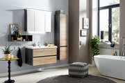 Modernes Badezimmer-Set mit wandhängendem Waschtischunterschrank in Holzoptik und Anthrazit, weißem Waschtisch, LED-Spiegelschrank und Hochschrank neben Badewanne am Fenster, Perspektive: frontale Raumansicht leicht von rechts.
