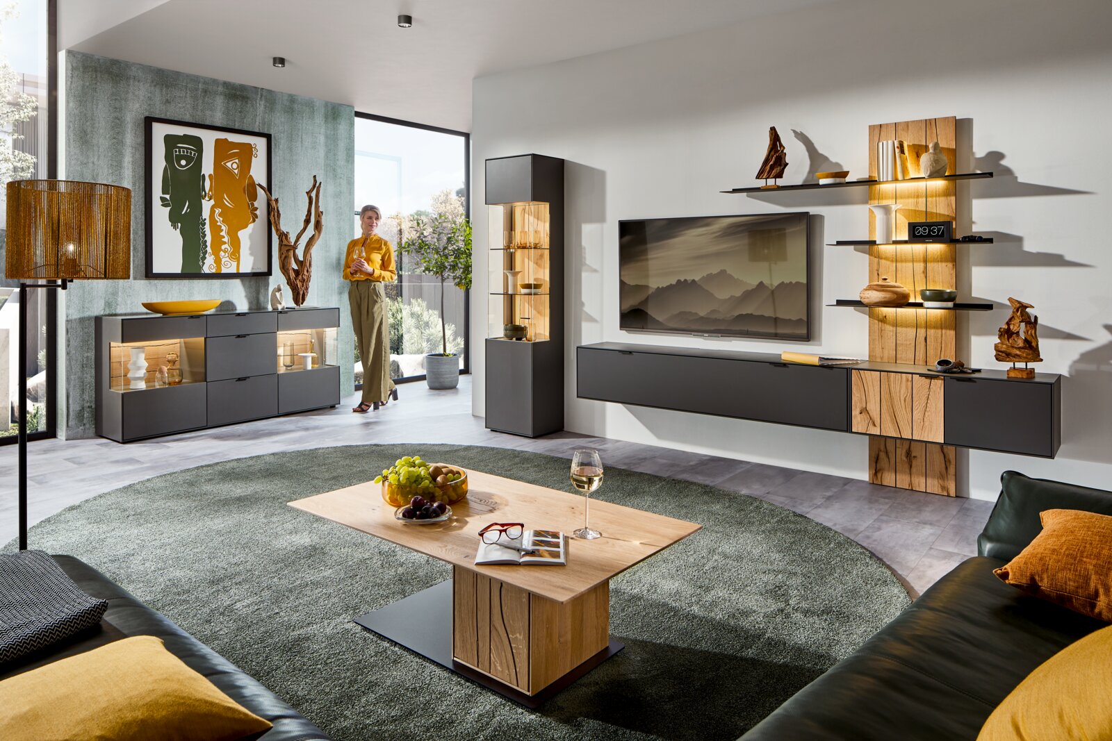 Moderne wandcombinatie voor de woonkamer met houten en glazen elementen, stijlvol ingericht, gezien vanuit een gezellige woonkamer met vloerkleed en salontafel.