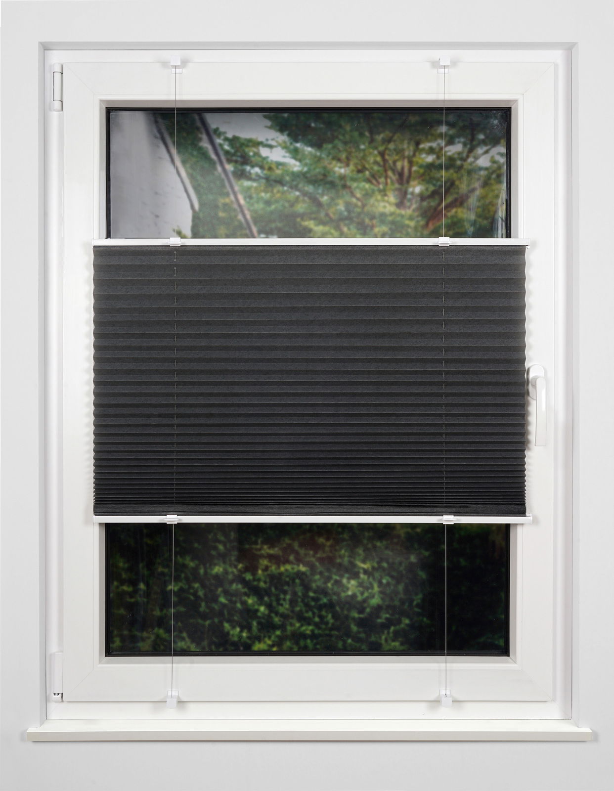 Schwarzes Plissee am Fenster, halb heruntergelassen, mit Blick auf einen Garten im Hintergrund.