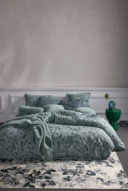 Bettwäsche-Set in sanftem Grün mit floralem Muster, frontal fotografiert, auf einem Bett mit mehreren Kissen und einer Decke arrangiert.