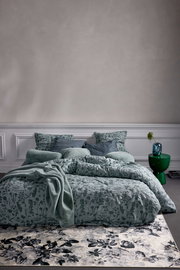 Bettwäsche-Set in sanftem Grün mit floralem Muster, frontal fotografiert, auf einem Bett mit mehreren Kissen und einer Decke arrangiert.