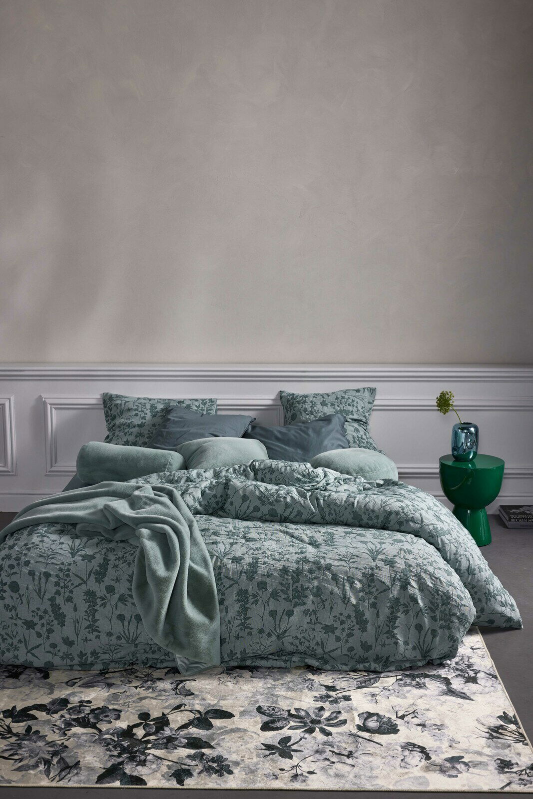 Bettwäsche-Set in sanftem Grün mit floralem Muster, frontal fotografiert, auf einem Bett mit mehreren Kissen und einer Decke arrangiert.