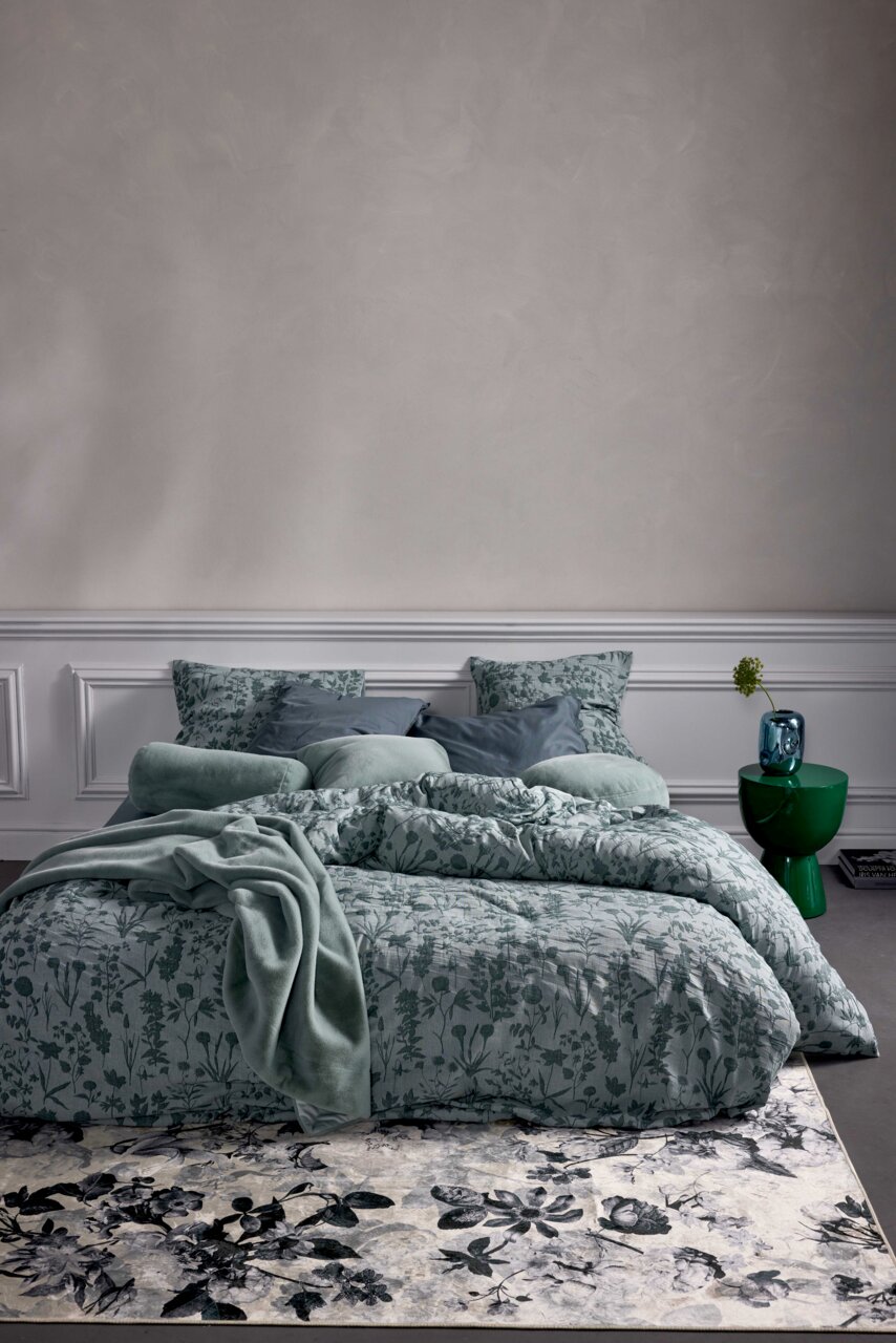 Essenza Home Beddengoed MARIBEL Beddengoedset in zachtgroen met bloemmotief, van voren gefotografeerd, opgemaakt op een bed met meerdere kussens en een deken.